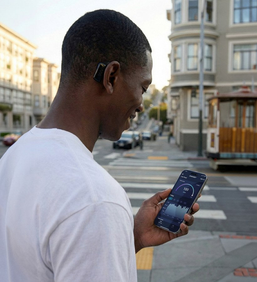 Man on a city street checking the AWEAR app's live calm score, device behind his ear