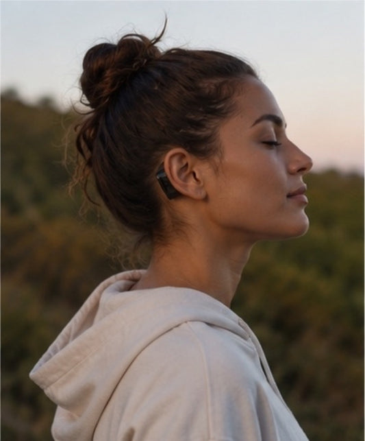 Woman outdoors at dusk, eyes closed and calm, wearing AWEAR behind the ear